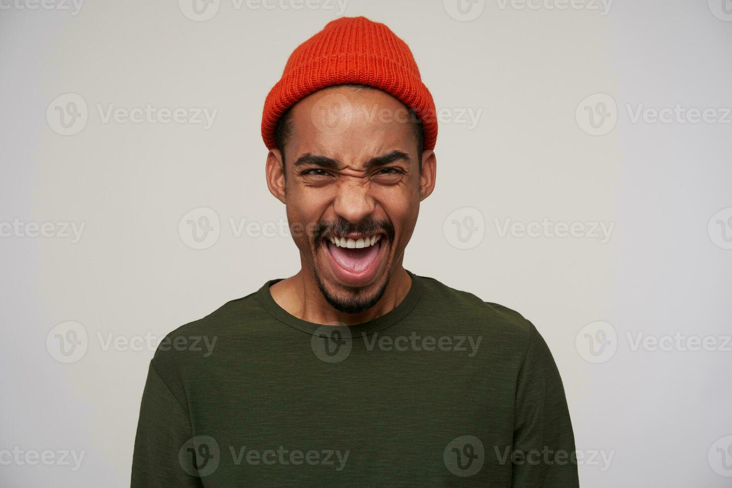 Excited young pretty dark haired bearded brunette man with dark skin screaming emotionally with wide eyes opened, wearing casual clothes while posing over white background photo