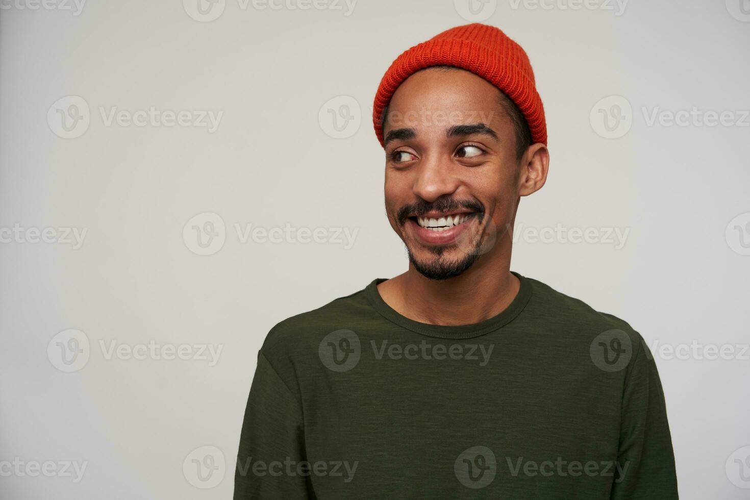 Cheerful young lovely dark skinned brunette hipster with beard looking positively aside with charming smile, rejoicing about meeting friends, isolated over white background photo