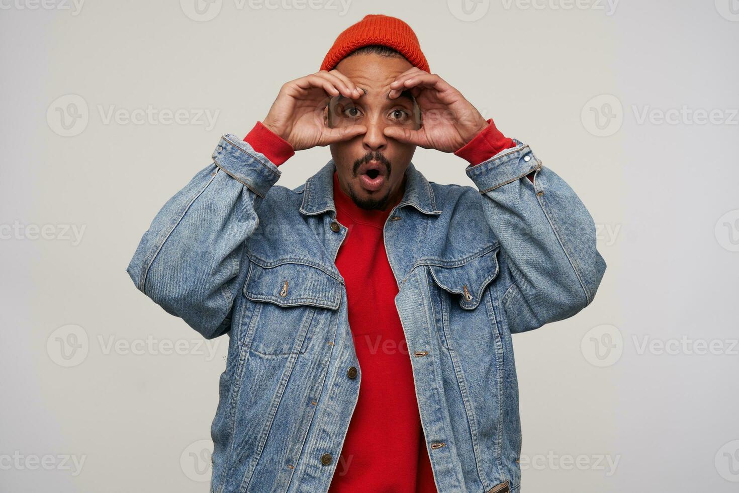 Studio shot of funny young dark haired bearded male with dark skin folding eyewear with raised hands and looking at camera, fooling while posing over white background photo