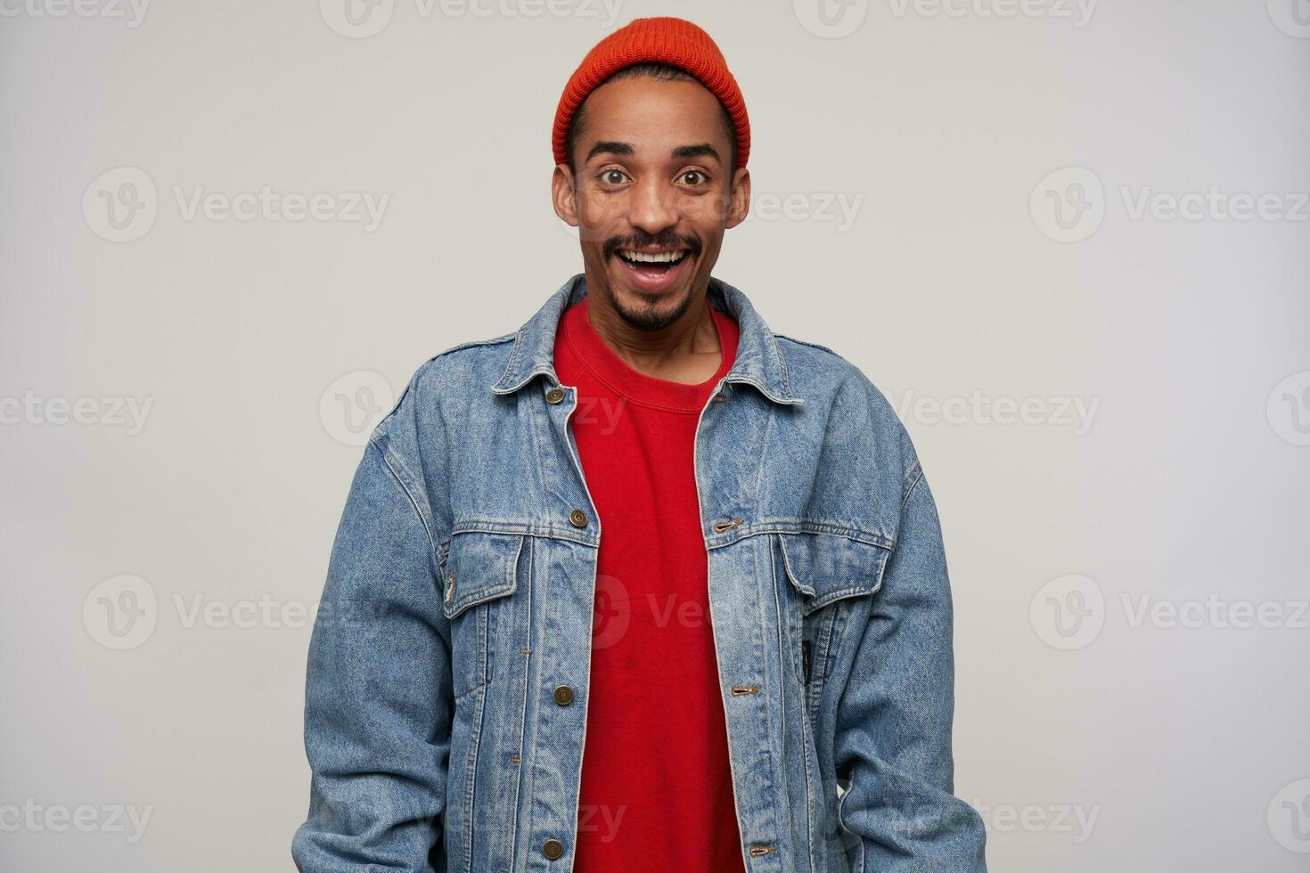 Indoor shot of cheerful attractive young brown-eyed bearded dark skinned guy looking happily to camera with wide smile, being in high spirit while standing over white background photo