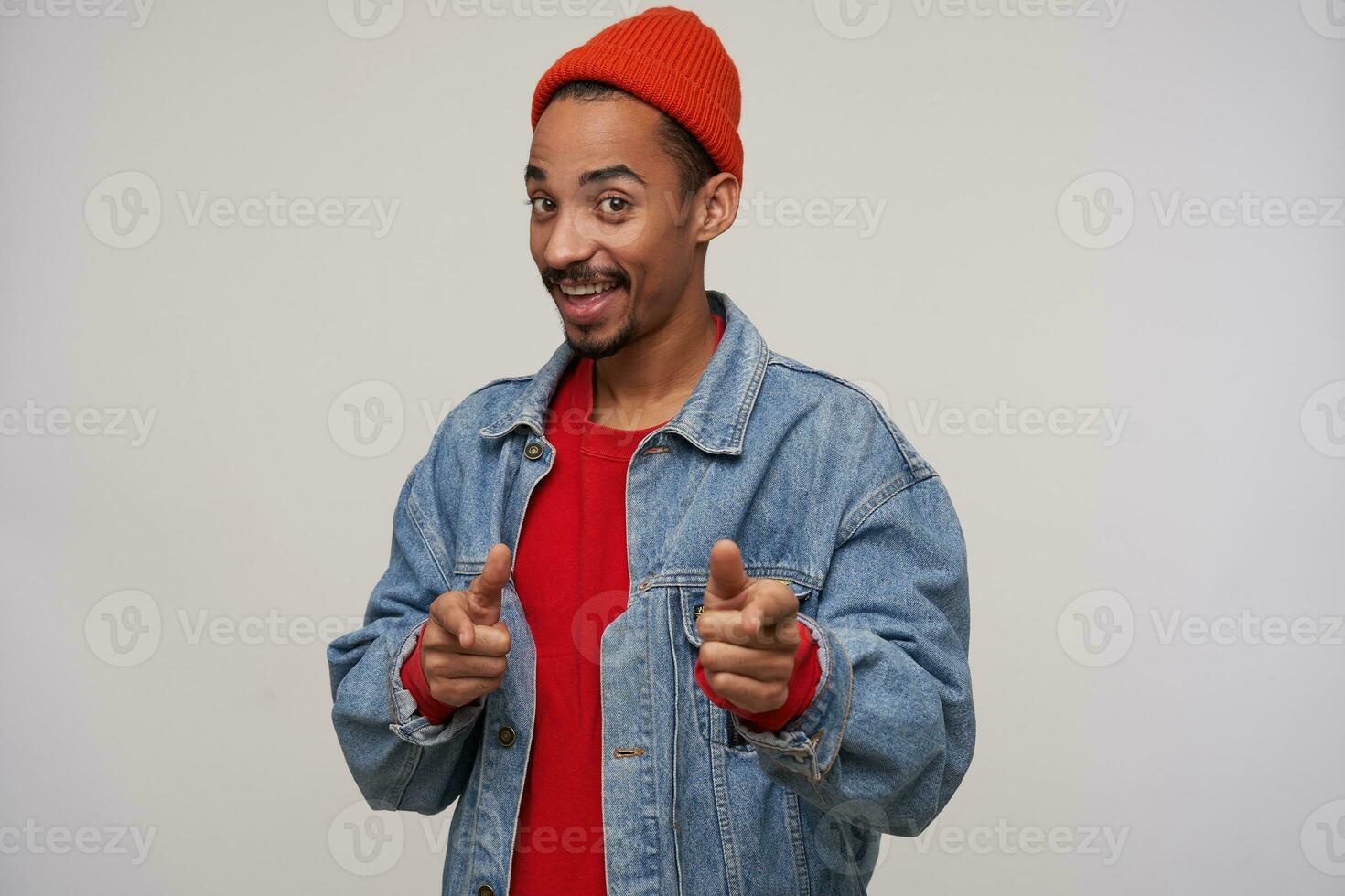 Positive young attractive dark skinned bearded guy dressed in casual wear while posing over white background, showing happily at camera with forefingers and smiling sincerely photo