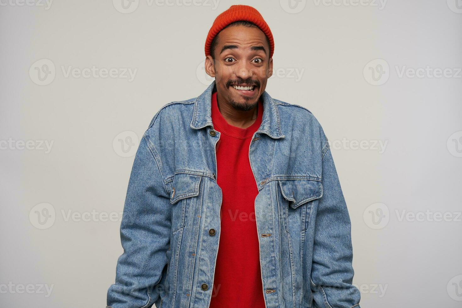 Cheerful young handsome bearded brown haired guy smiling happily and biting underlip, raising excitedly eyebrows while posing over white background in casual wear photo