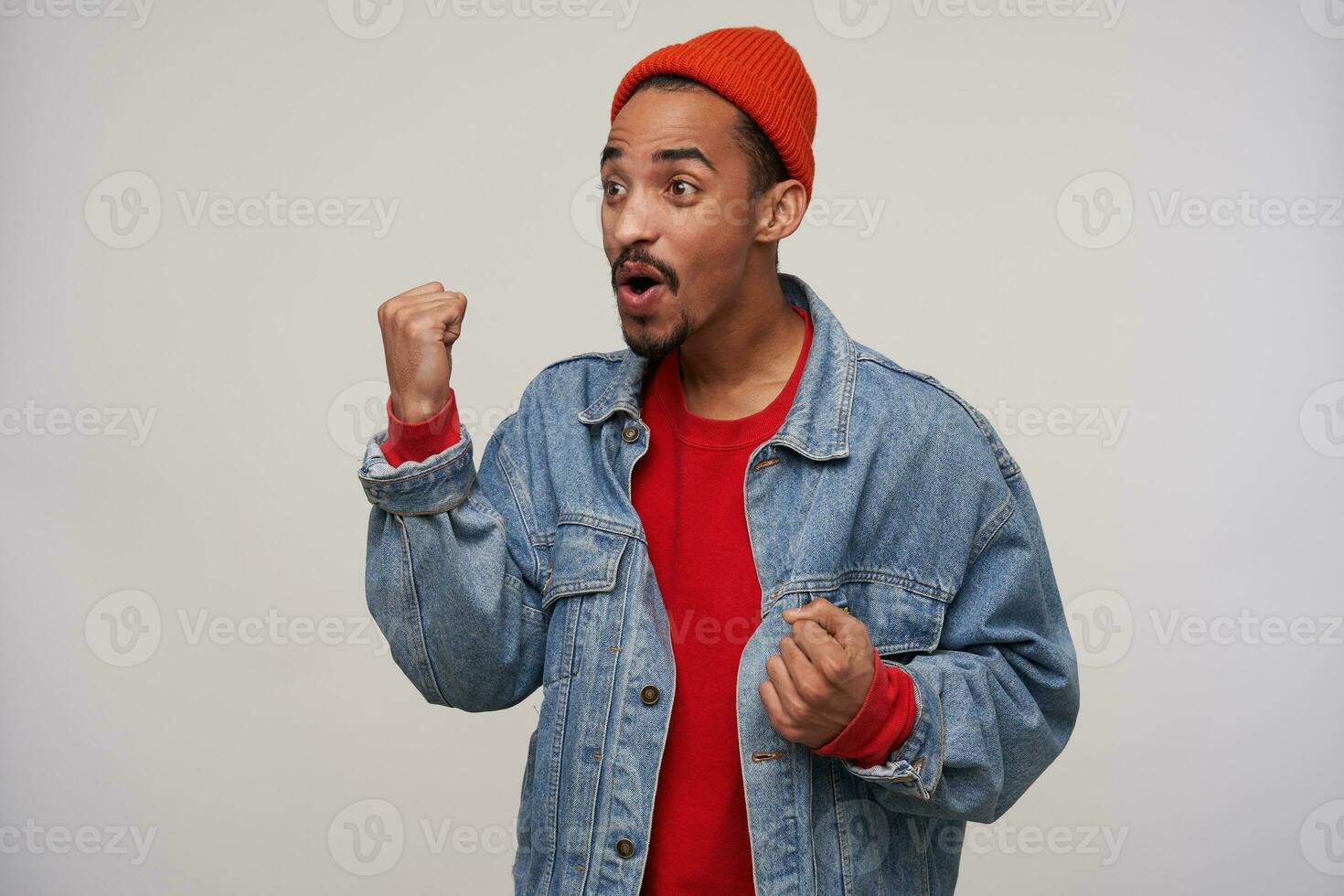 Excited young lovely dark skinned brown haired man dressed in casual wear while posing over white background, looking cheerfully aside and raising fists happily photo