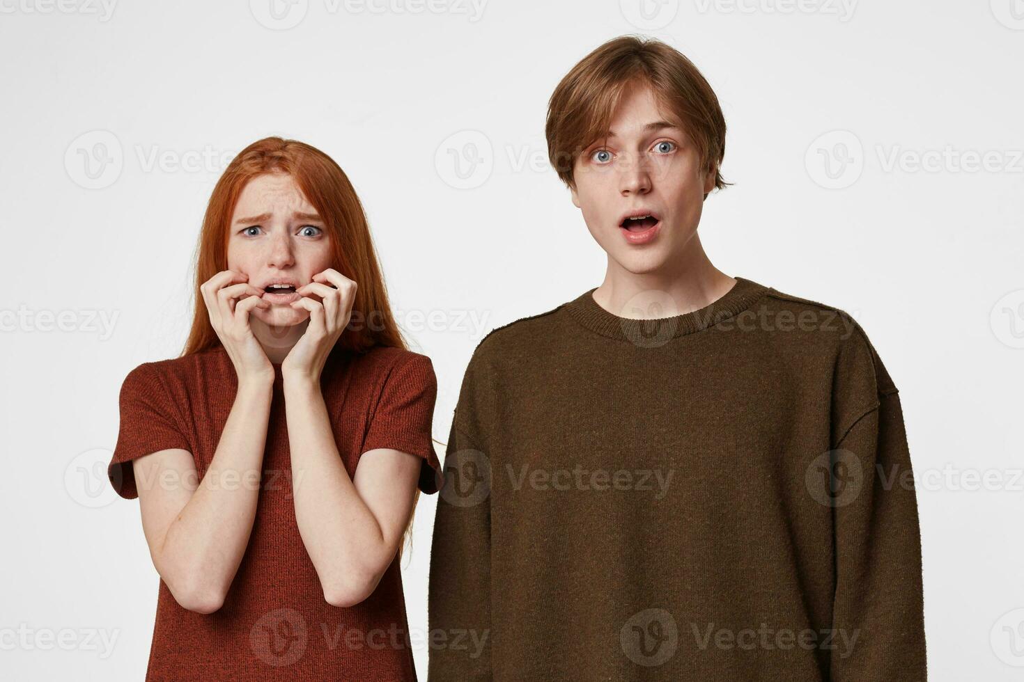 ouple of a guy and a girl, casually dressed, stand frightened, shocked, surprised, female holds her hands near her face, man stares with his mouth open, over white background photo