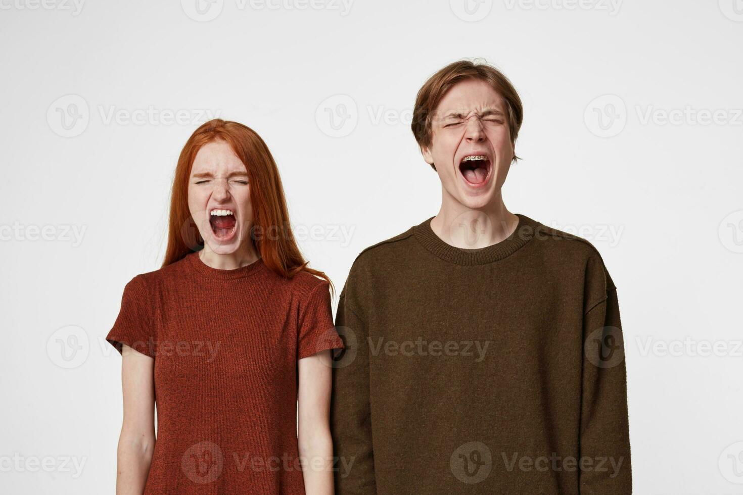 Close up of scared boy and girl,feel frightened afraid, mouth wide openes as screaming shouting yelling loud, eyes closed, over blue background photo