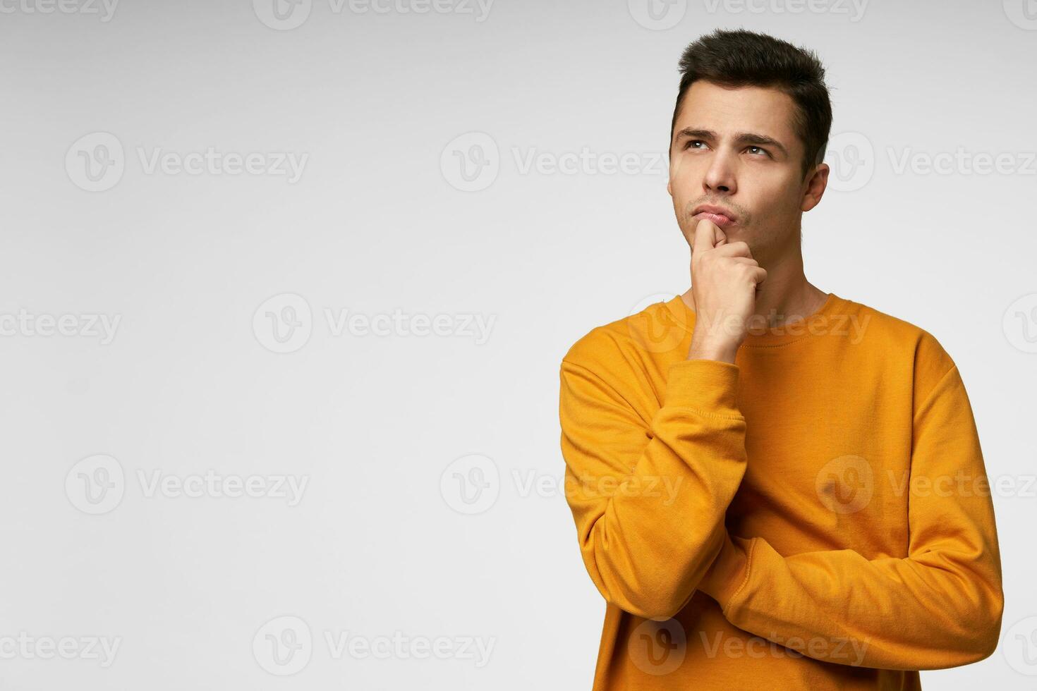 Waiting for inspiration. Thoughtful young man holding hand on chin and looking away standing isolated over white background. Copy space for advertisement photo