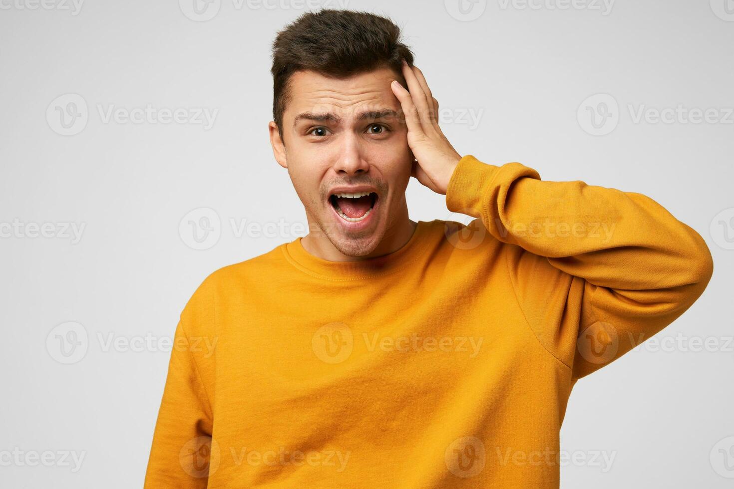 Close up of screaming man holding his head, mouth opened, watching crash, feeling panic, looks helpless, dressed casually, isolated over white background photo
