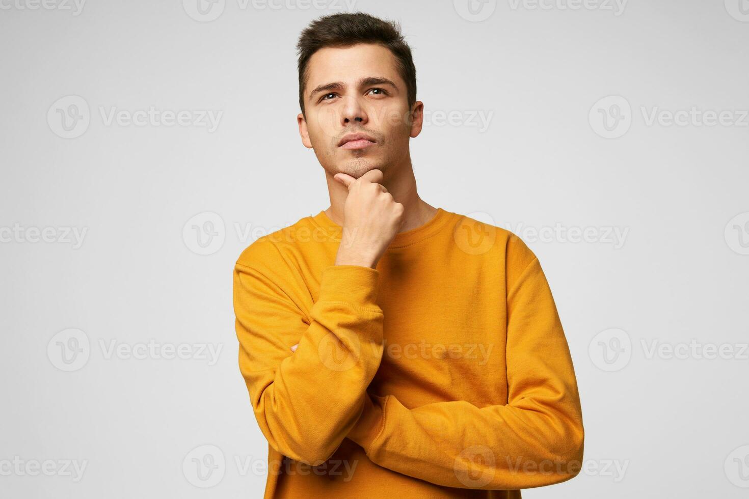A handsome guy looks into the distance up, his head slightly raised, holding his chin, thinks about his future, make plans, dreams, feels confident in his abilities, isolated over white background photo