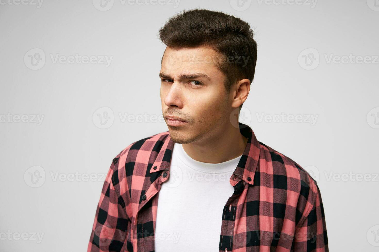 Attentive young man looks suspiciously standing in a half-turn as if he is peeping or overhears, has an incredulous look, isolated over white background photo