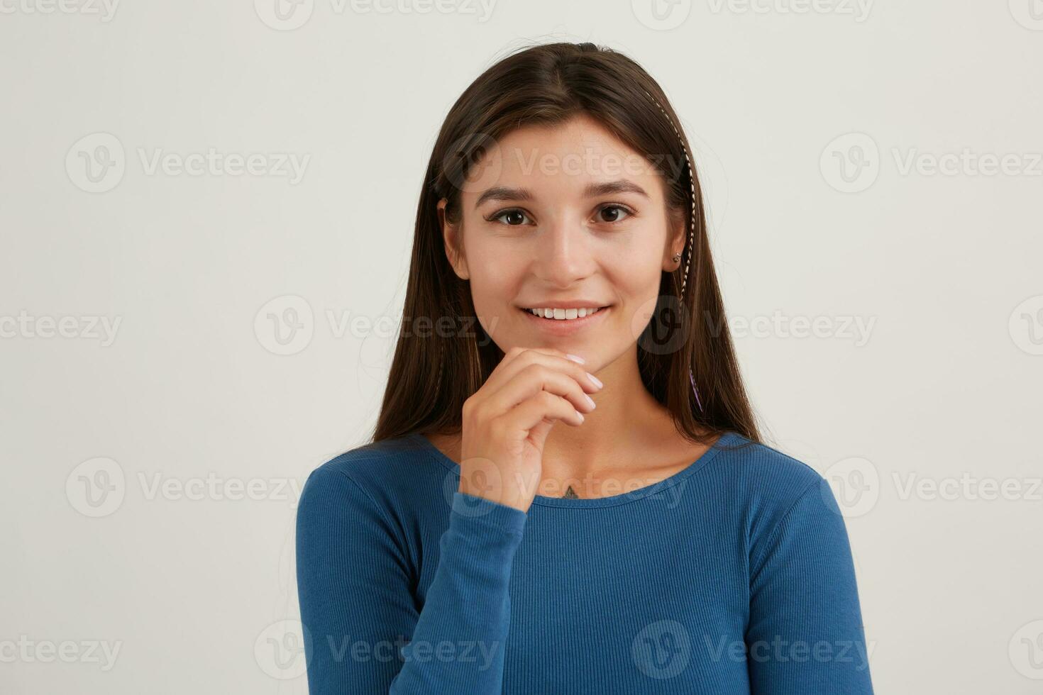 Positive lady, pretty woman with dark long hair. Wearing blue jumper. Emotion concept. Touching her chin and smiling. Watching at the camera isolated over white background photo