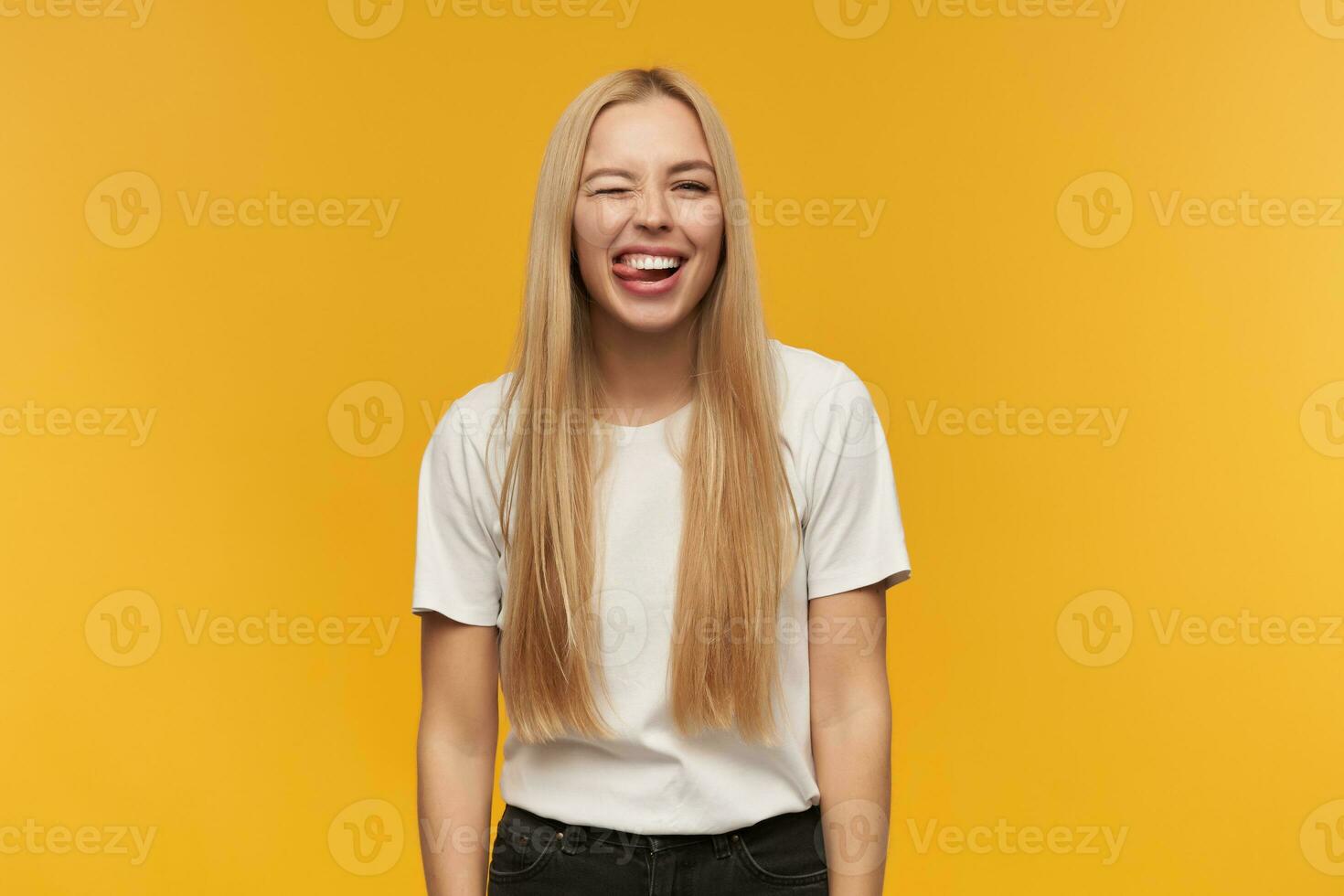 Portrait of attractive, adult girl with blond long hair. Wearing white t-shirt and black jeans. People and emotion concept. Watching at the camera, isolated over orange background photo