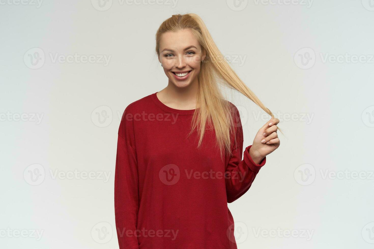 Nice looking woman, beautiful girl with long blond hair. Wearing red sweater. People and emotion concept. Watching at the camera, isolated over white background photo