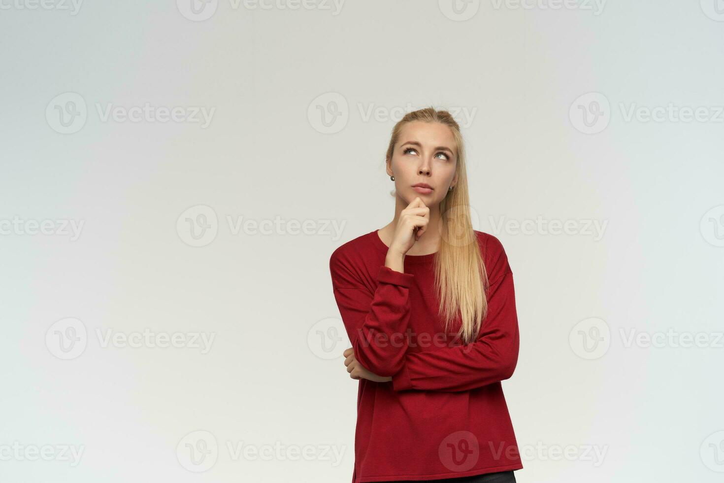 Portrait of attractive, adult girl with blond long hair. Wearing red sweater. People and emotion concept. Watching up thoughtfully at copy space, isolated over white background photo