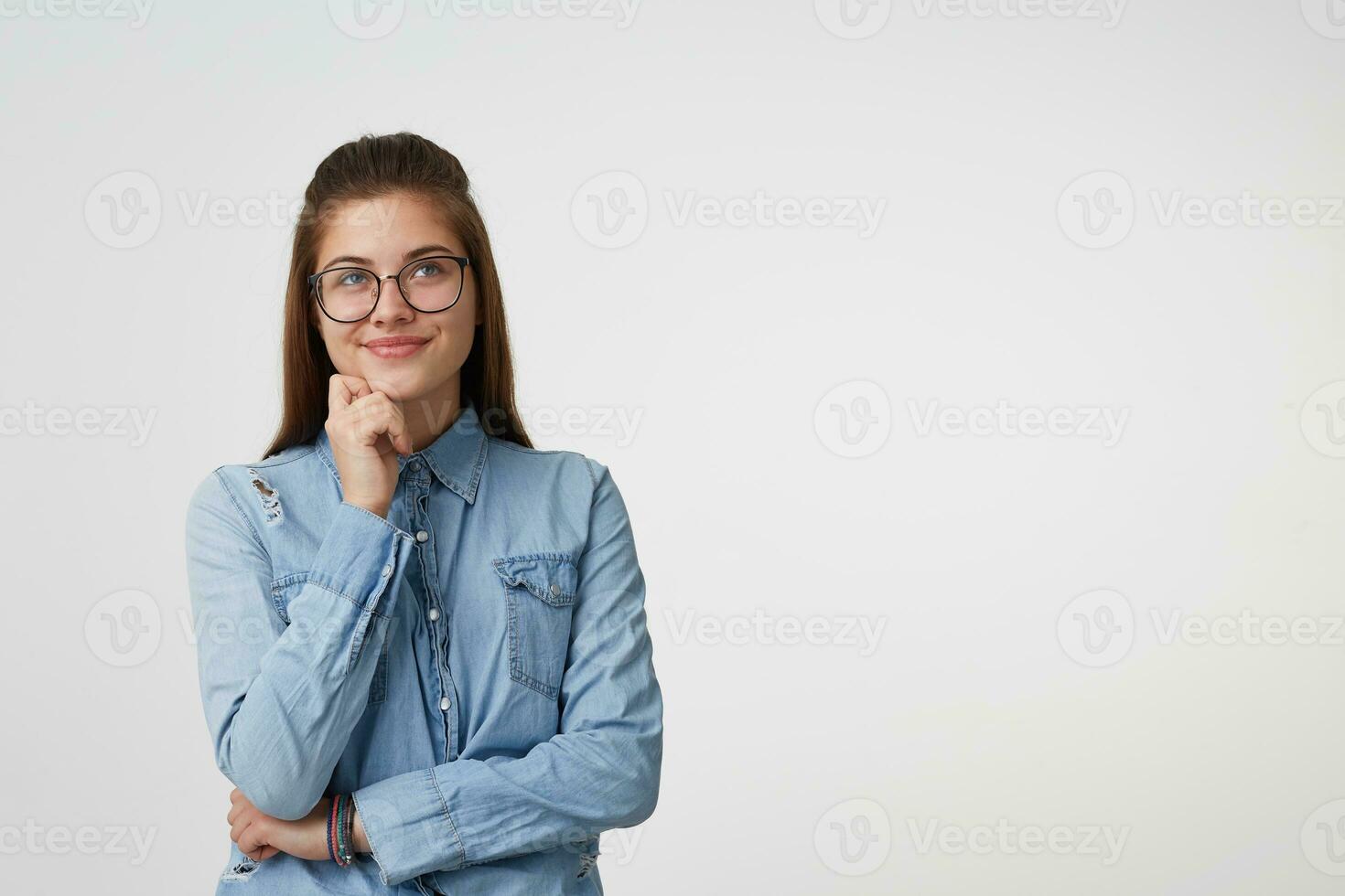 Girl with a dreamy look, looks into the distance holds one hand near the chin the second crossed stands isolated on a white background next to copy space for advertisement promotion photo