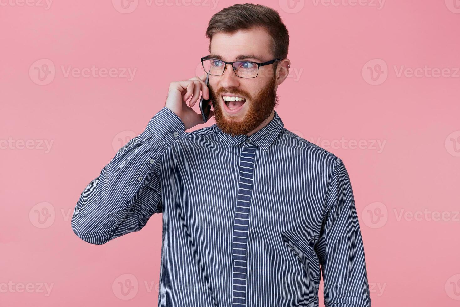Photo of serious smiling happy successful bearded man with glasses calling with his phone, smiles broadly, happy amazed, isolated on a pink background.