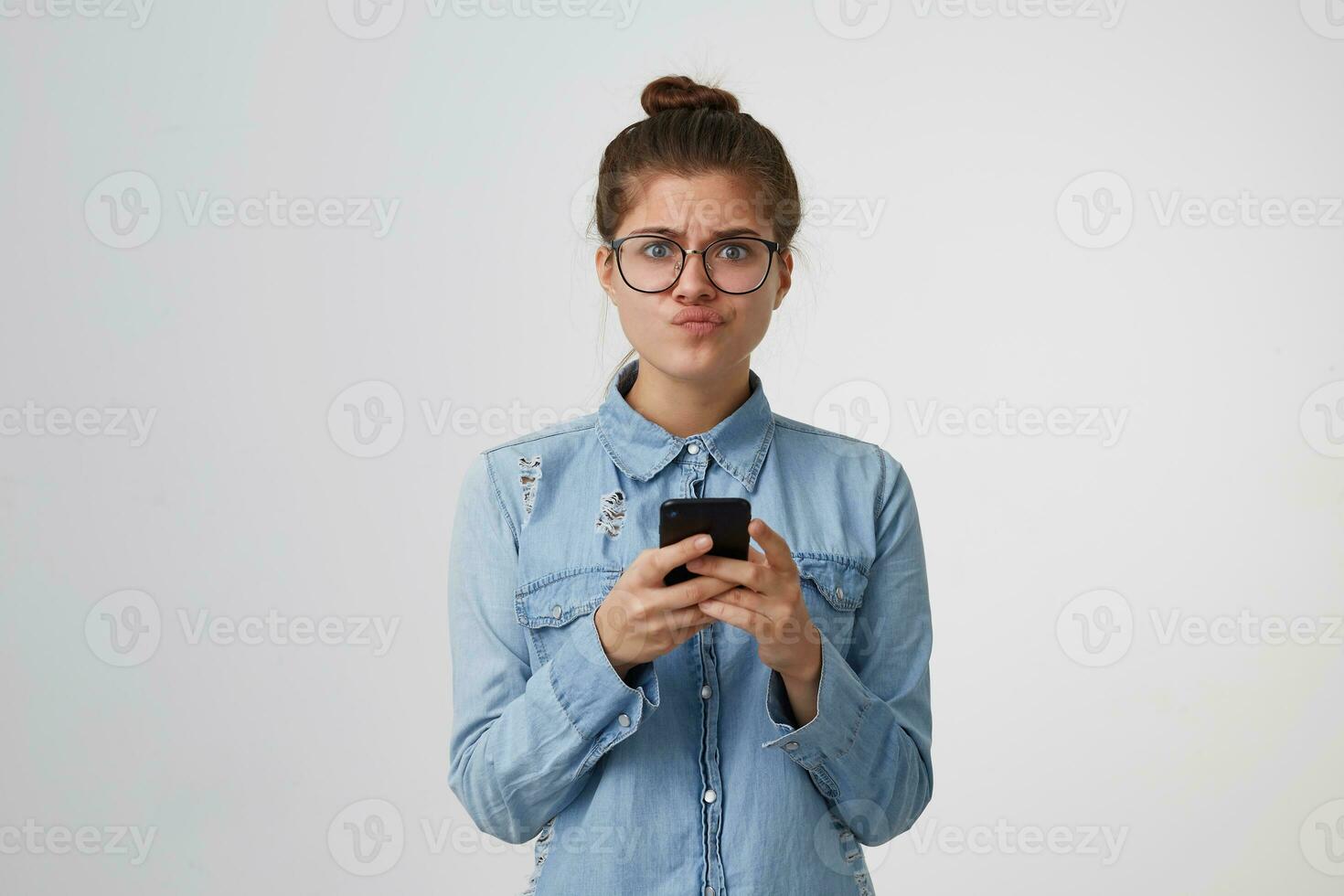 The girl looks with displeasure at the camera, puffed up her lips, disappointed, holds smartphone in hands, someone did not live up to her expectations, got upset after the message,on white background photo