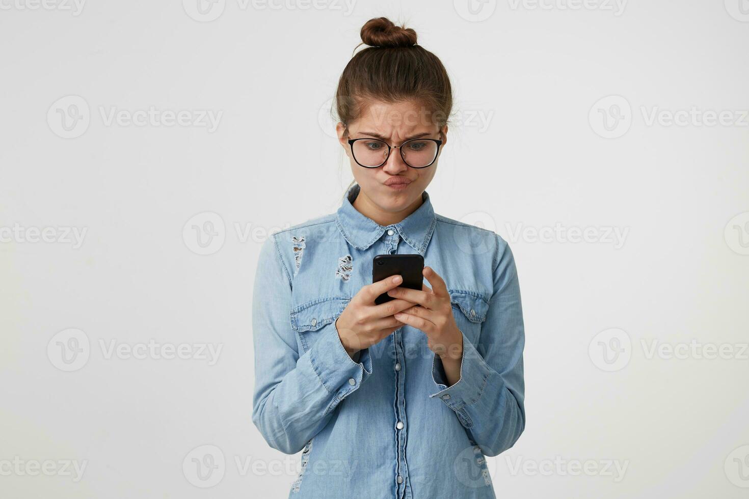 Young woman looks with displeasure at the smartphone in hands, puffed up her lips, disappointed, someone did not live up to her expectations, got upset after the message,on white background photo
