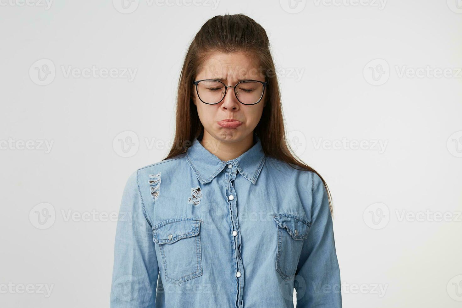 un muy triste joven adolescente niña cerrado su ojos, llorar, convertido fuera su labio, trastornado ofendido ofendido, vestido en un mezclilla camisa, aislado en un blanco antecedentes. foto