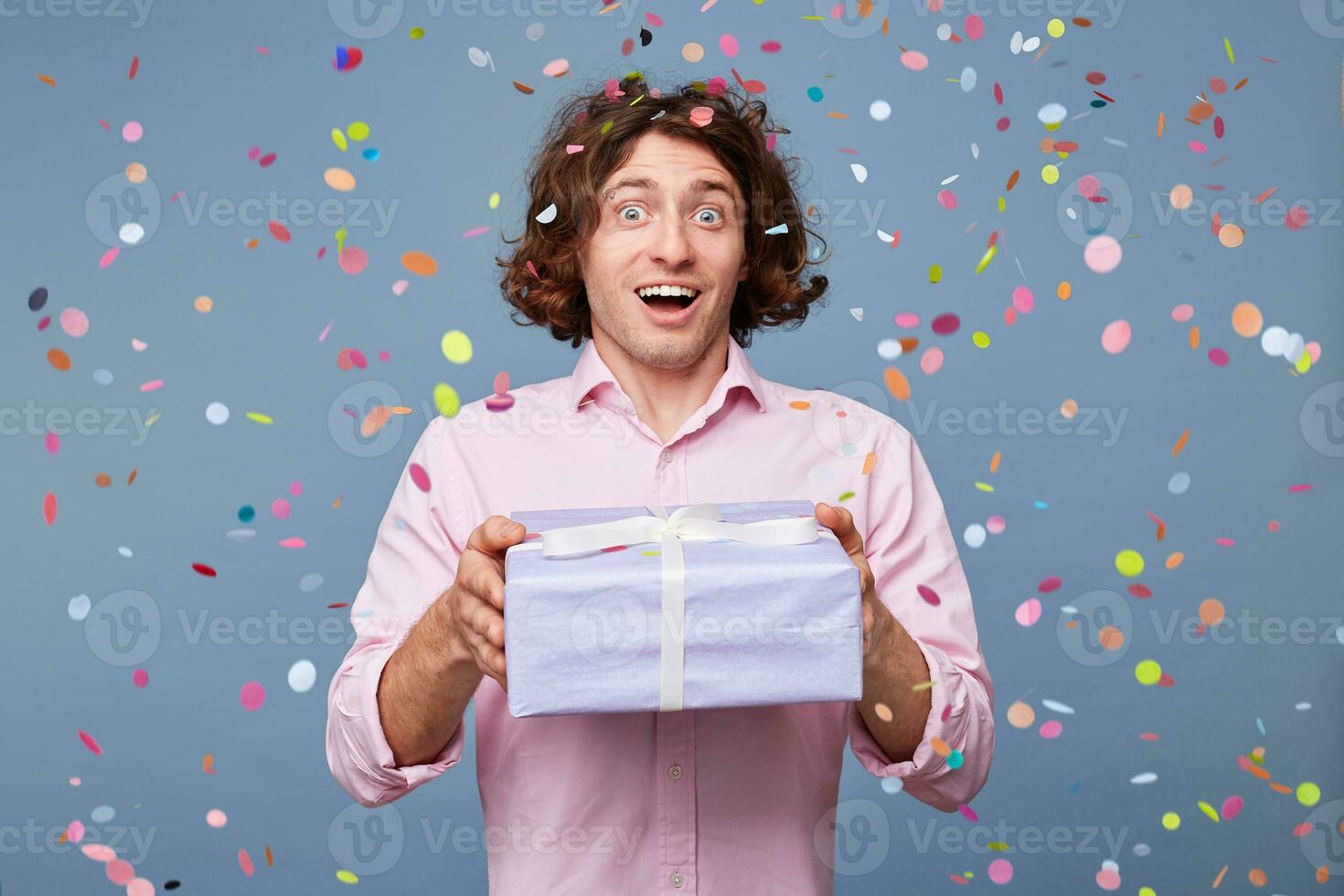 Birthday man accepts congratulations, gets a gift in a big box, on the face expression of amazement, joy, happiness, pleasure, eyes and mouth wide open, confetti falling down. photo