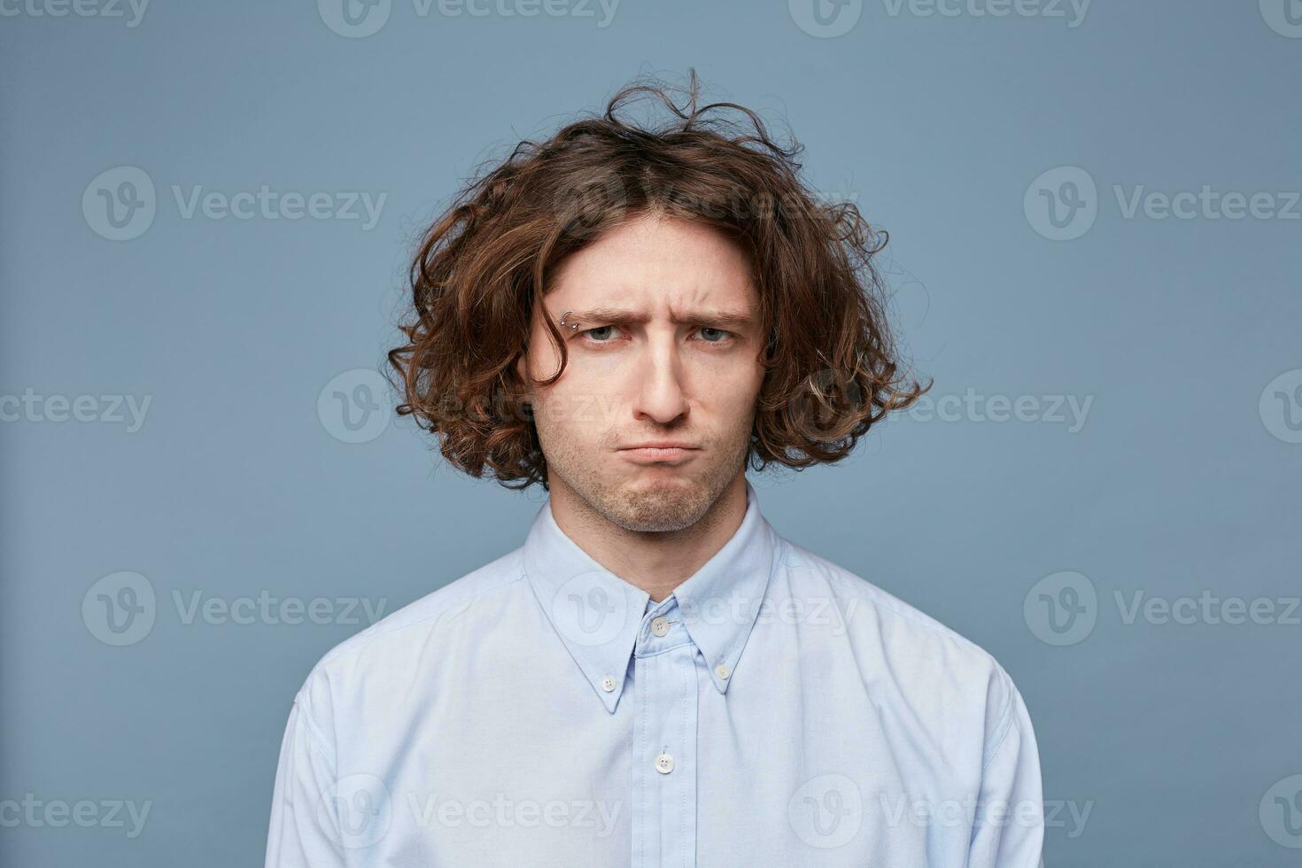 Portrait of a guy with a frustrated expression, frowning eyebrows, pursed lips, dissatisfied, upset, offended, looking into the camera standing against blue background. photo