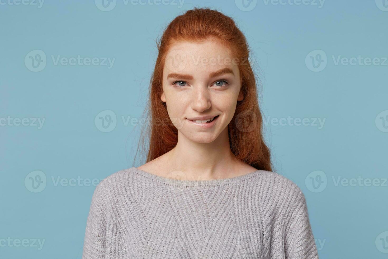 Clever sly red-haired girl ponders a plan, plans an adventure, came up with something extraordinary, isolated on a blue background photo
