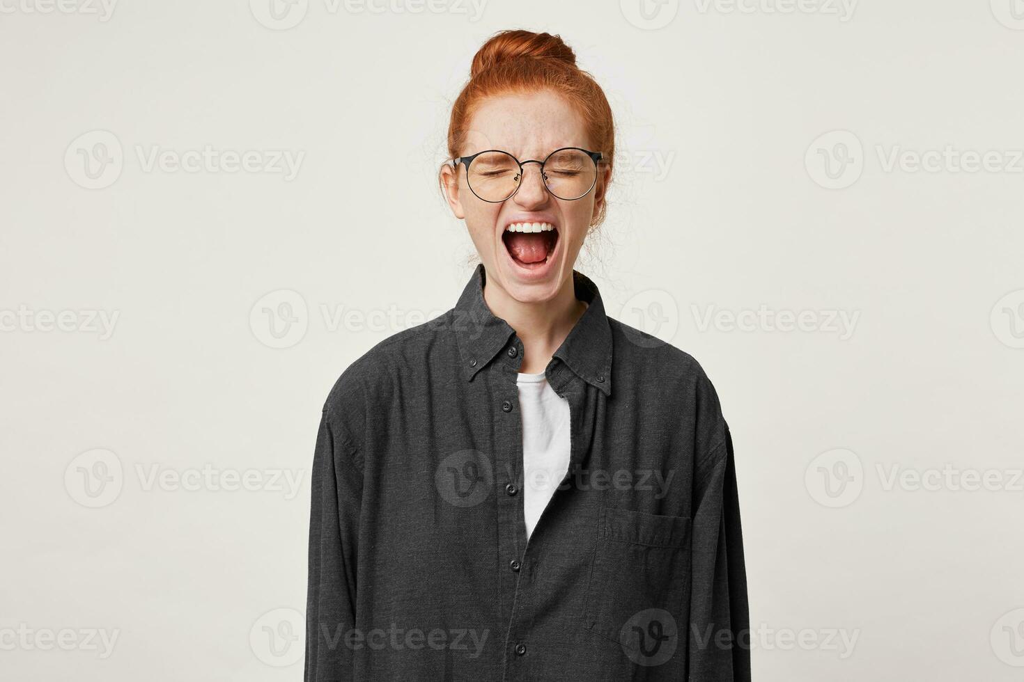 Close up of scared red-haired girl, feels frightened afraid, mouth wide opened as screaming shouting yelling loud, eyes closed, over white background photo