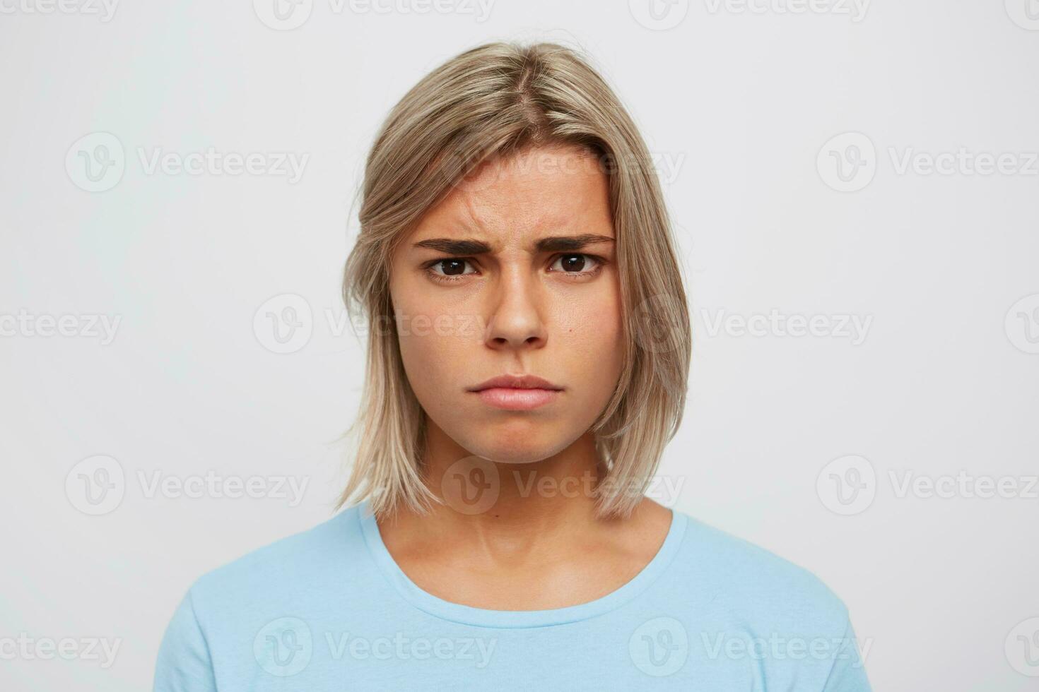 Closeup of worried serious young woman with blonde hair wears blue t shirt and feels stressed isolated over white background photo