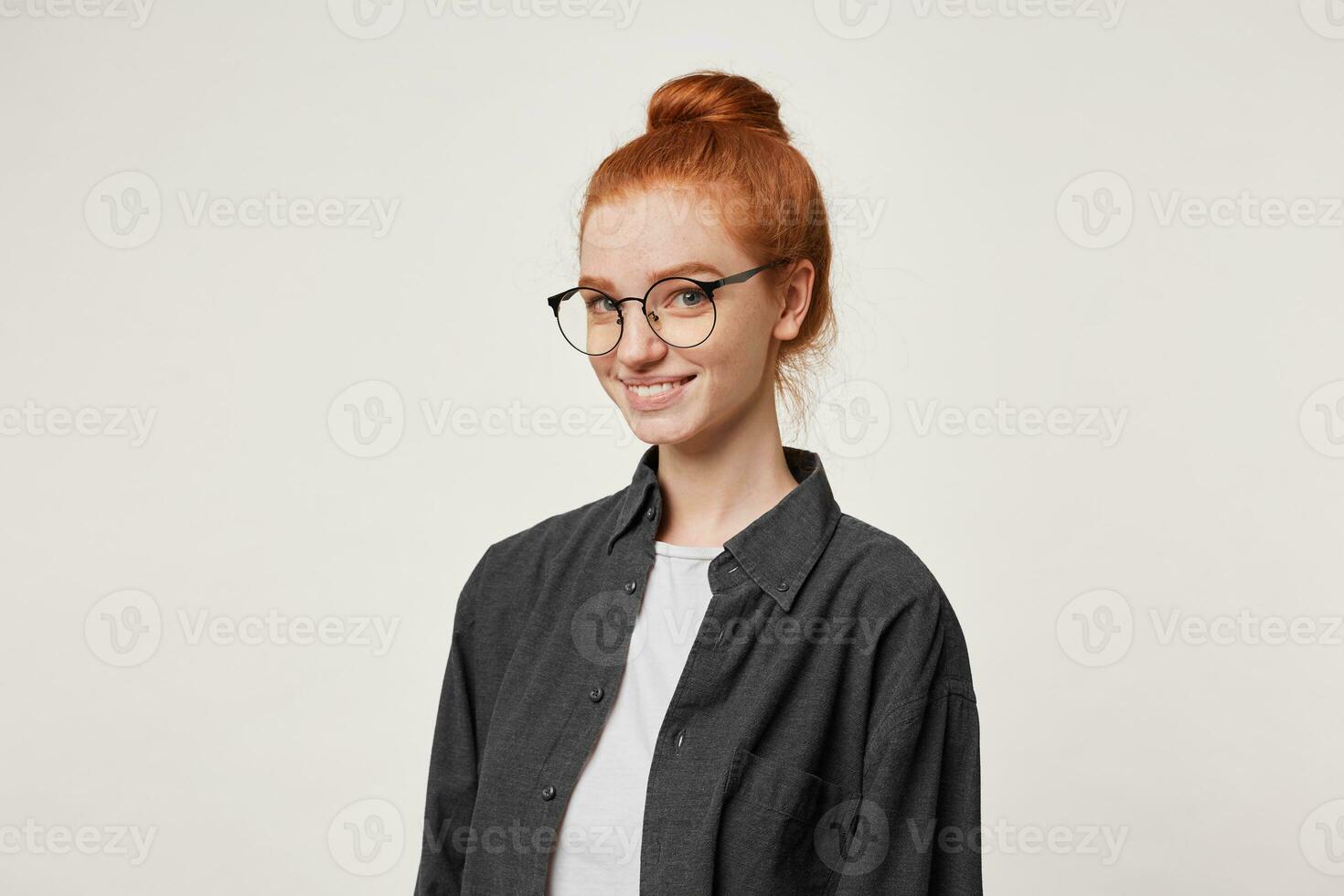 un joven Pelirrojo niña soportes en un media vuelta mirando a el cámara mediante gafas.alegre joven mujer vestido en un negro del hombre camisa es sonriente afablemente aislado en un blanco antecedentes. foto