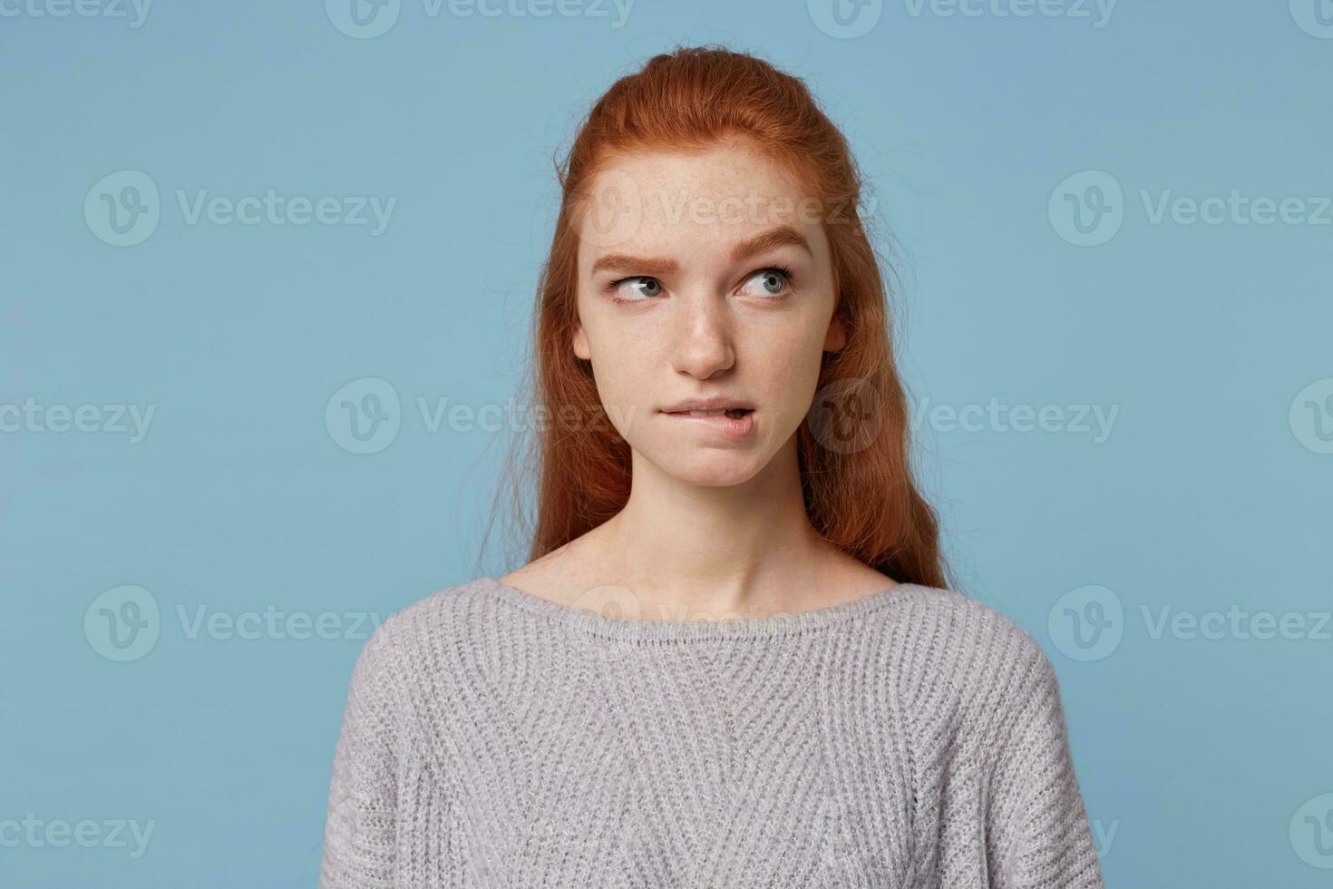 retrato de un joven Pelirrojo adolescente niña mira lejos poco su inferior labio, dudas, piensa terminado opciones, es inseguro, plagado por dudas, aislado en azul antecedentes foto