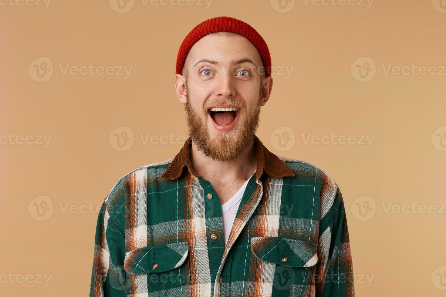 Happy excited bearded man in red hat isolated over beige background. Shocked with excellent results of final game of favourite football team photo