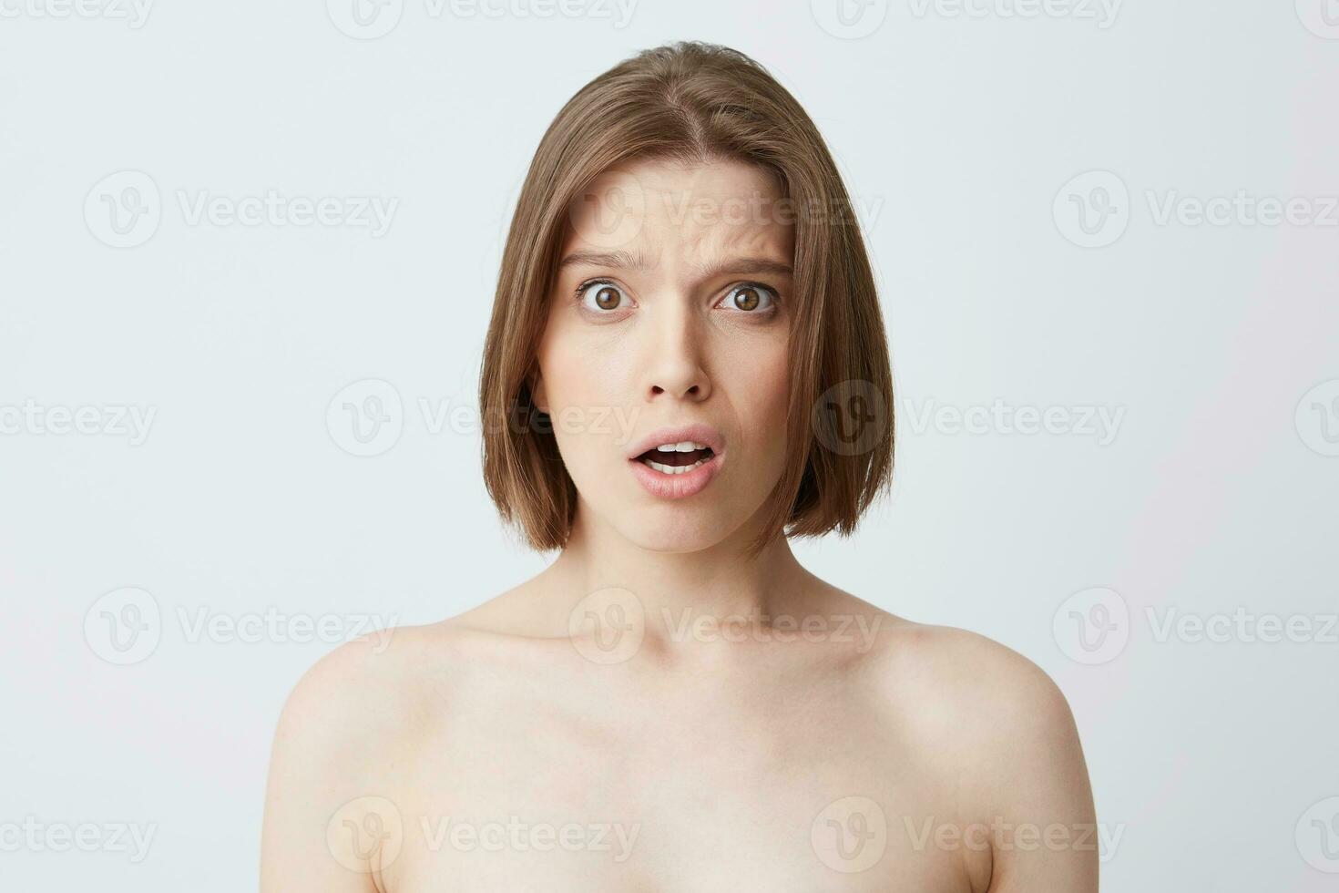 Cropped shot of amazed embarresed young woman with dark hair and healthy skin feels confused and surprised isolated over white background Standing half naked after shower photo
