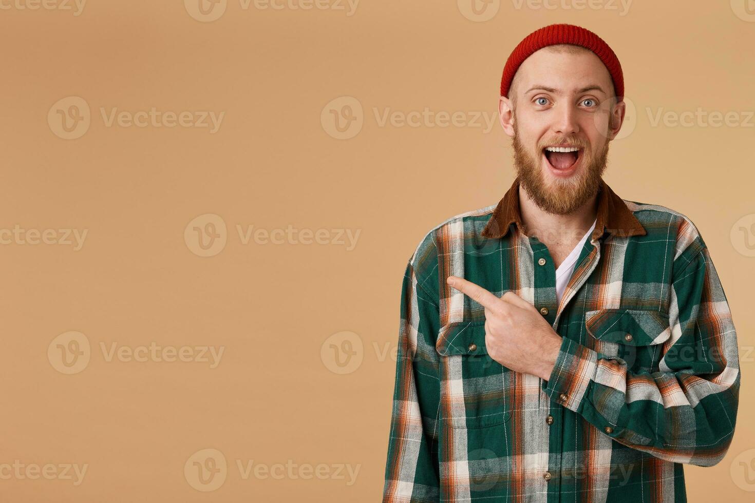 Indoor shot of amazed excited man feels successful, pointing at left corner on blank copy space, dropping jaw standing rightside isolated over beige background, says omg or wow. photo