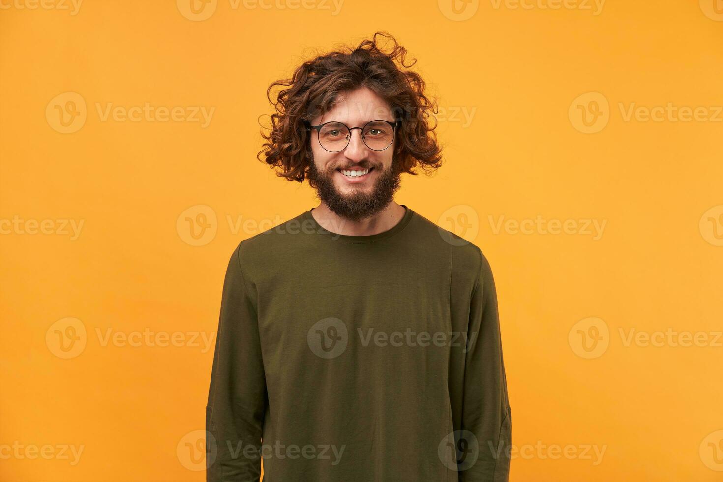 Cute friendly bearded man in glasses with curly hair smiling looks happy isolated on yellow background. A good friend came to visit, a niceguy. photo