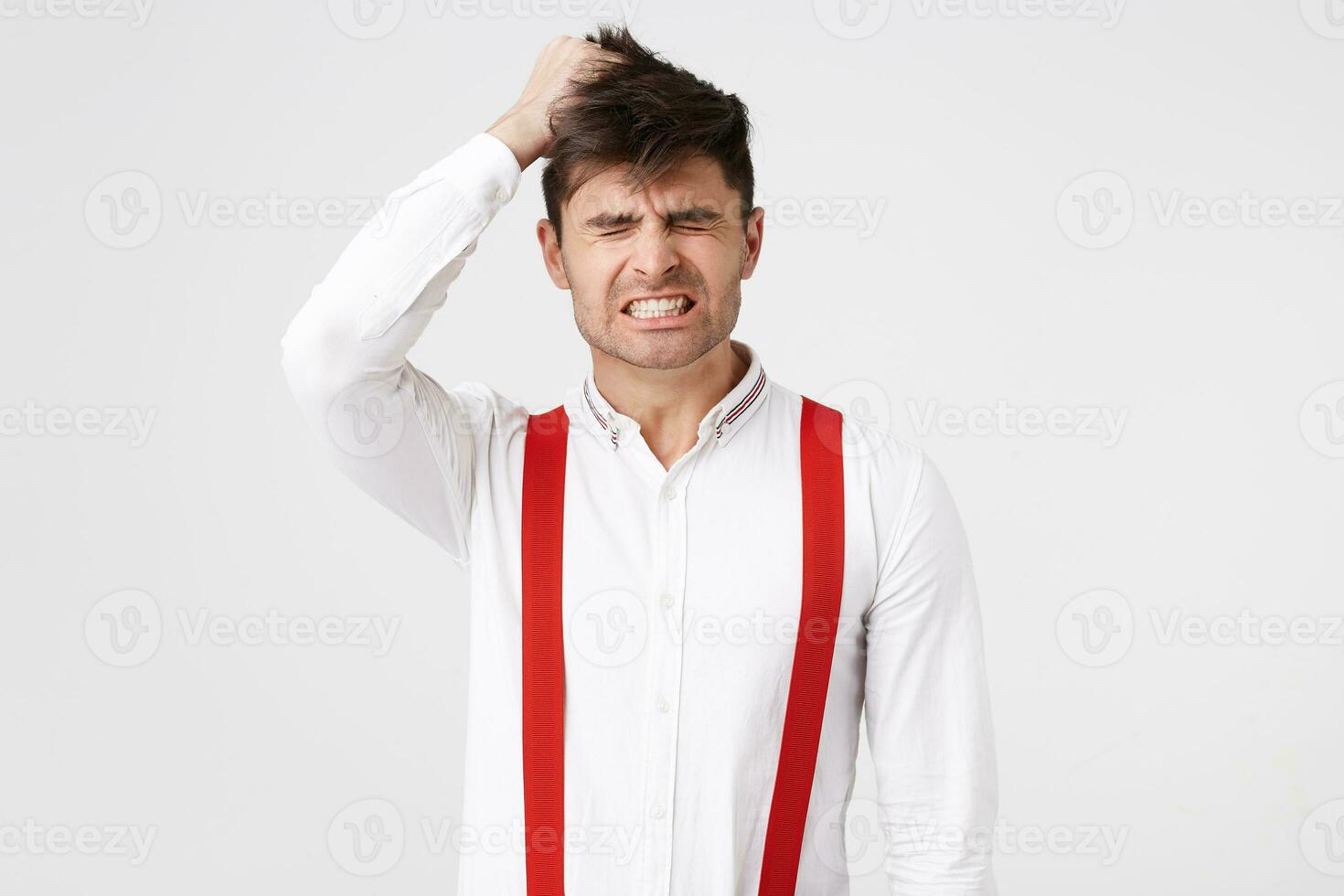 Shocked dark hair unshaved man, looks frightened of the catastrophe, crash, disaster, of her actions, gritting his teeth, hand clutched at his head, hair tousled, over white background photo