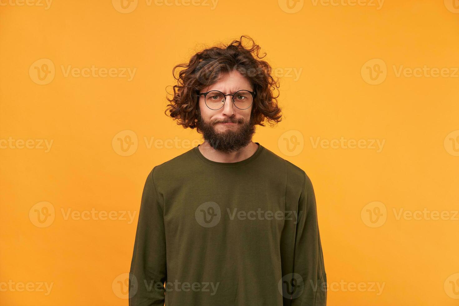 A bearded man in glasses with dark curly hair looking at the camera with a frustrated expression of his face, pursed his lips. Displeased with the result. Expecting more. photo