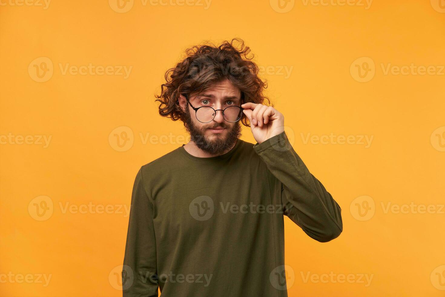 Tthe young professor lowers his glasses with interest and examines something new. Bearded curly-headed man looked something curious and takes off his glasses photo