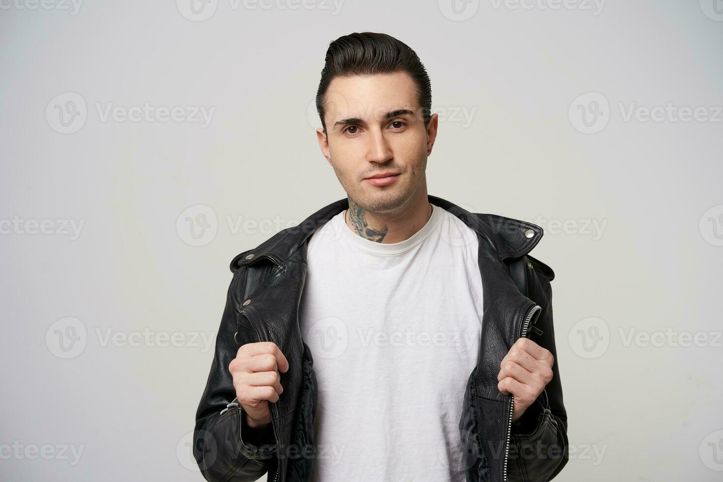 Rebel, attractive guy with a stylish haircut and styling with a grease, tattoo on the neck,keeps hands like putting down black rocker-style leather jacket and leaving blank white T-shirt photo