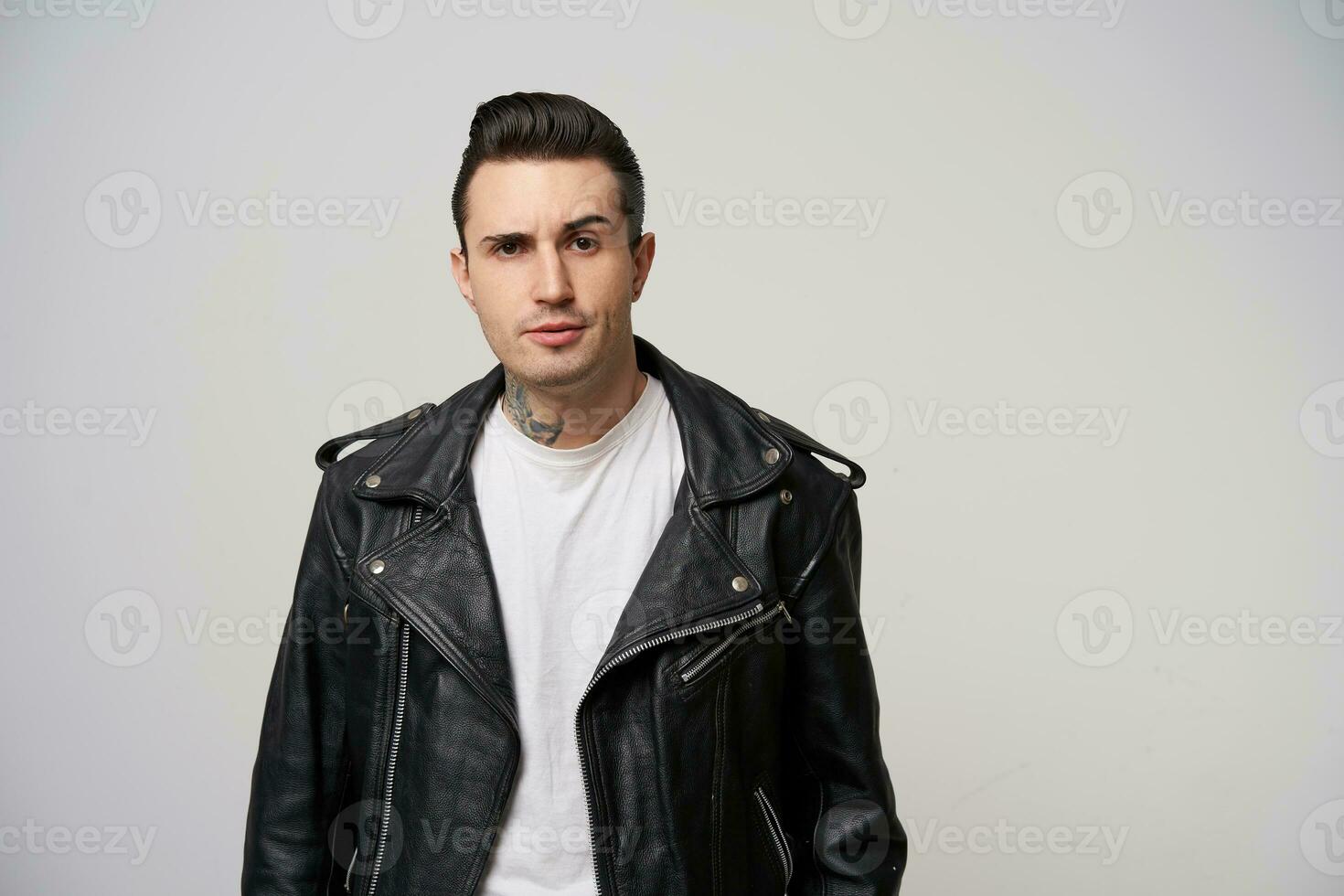 playing eyebrows, looks dissatisfied, annoyed, motto racer with a stylish hairstyle in briolin, tattoo on the neck, looks in the style of 50s-60s in black leather jacket, feels uncontentious photo