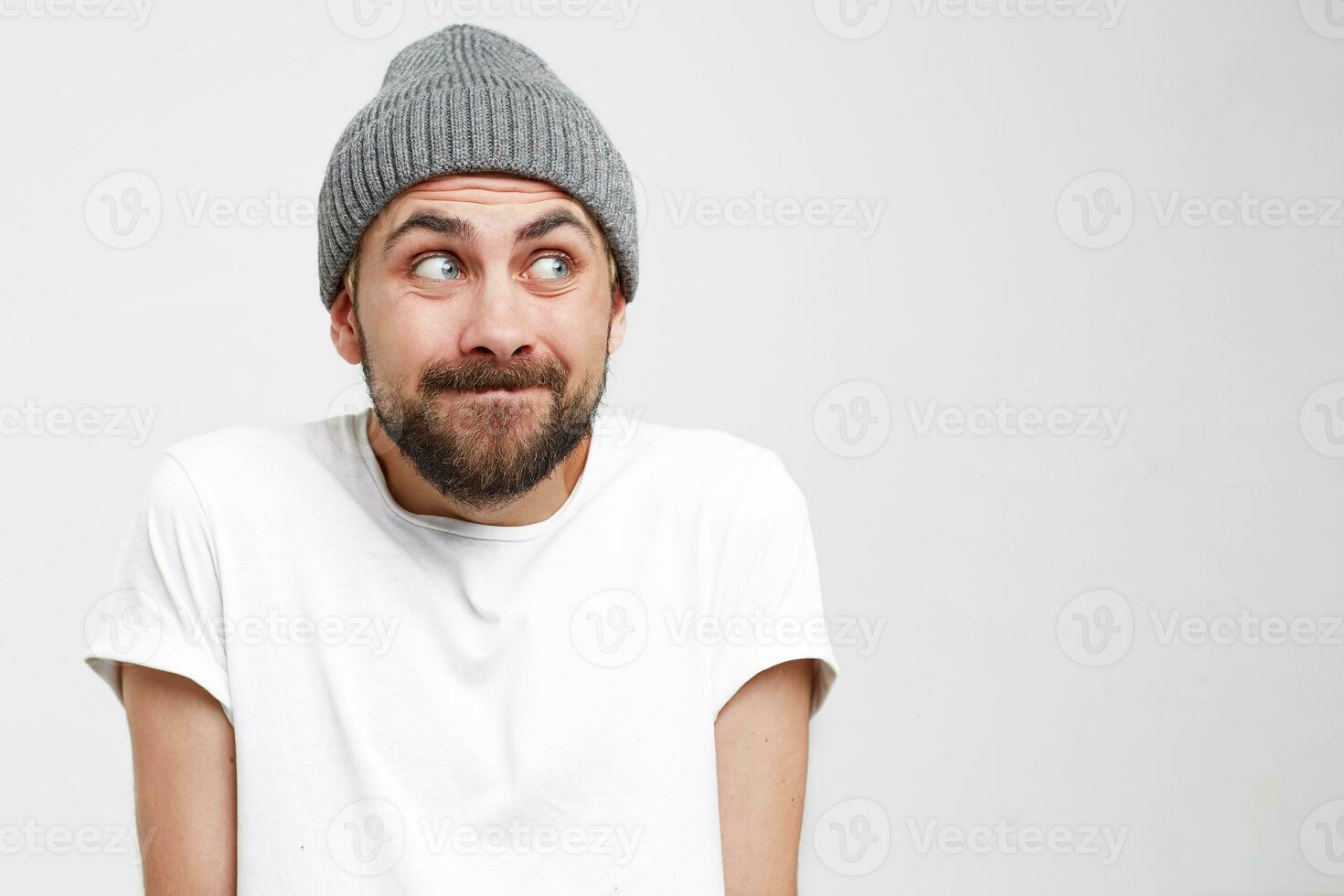 Headshot of a young man with a beard, pressed his head into shoulders and looked away to the side, making excuses or verbally defending himself, puzzled and apologizing, as if saying It was not me. photo