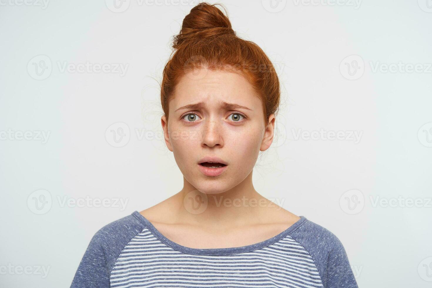 Frightened young redhead pretty woman frowning her eyebrows while looking confusedly at camera, keeping her hands down while posing over pink background photo
