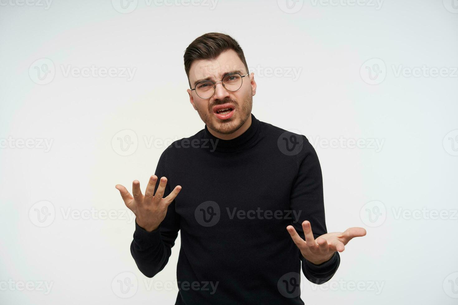 Puzzled young handsome unshaved brunette man raising confusedly hands and grimacing his face while looking at camera, standing over white background photo