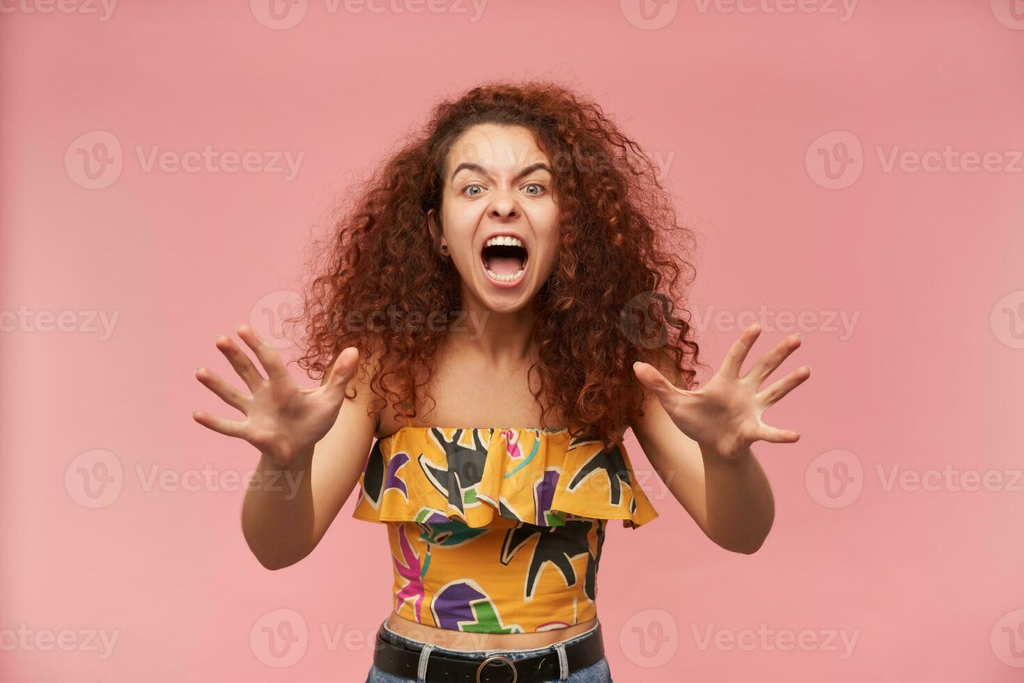 retrato de enojado, pelirrojo niña con Rizado cabello. vistiendo vistoso fuera del hombro blusa. personas y emoción concepto. Molesto apagado, tenido suficiente. acecho a el cámara aislado terminado pastel rosado antecedentes foto