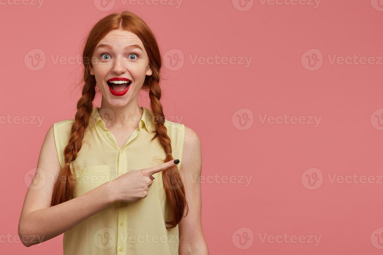 Indoor portrait of young ginger female with freckles posing over pink background photo