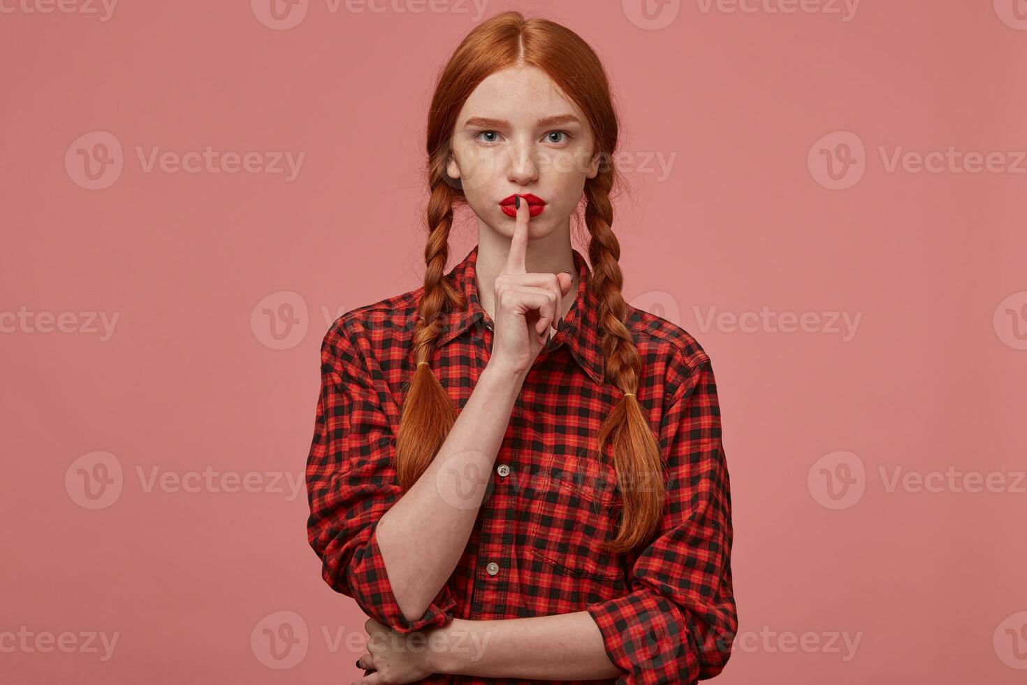 indoor shot of serious ginger female, showing silence gesture. photo
