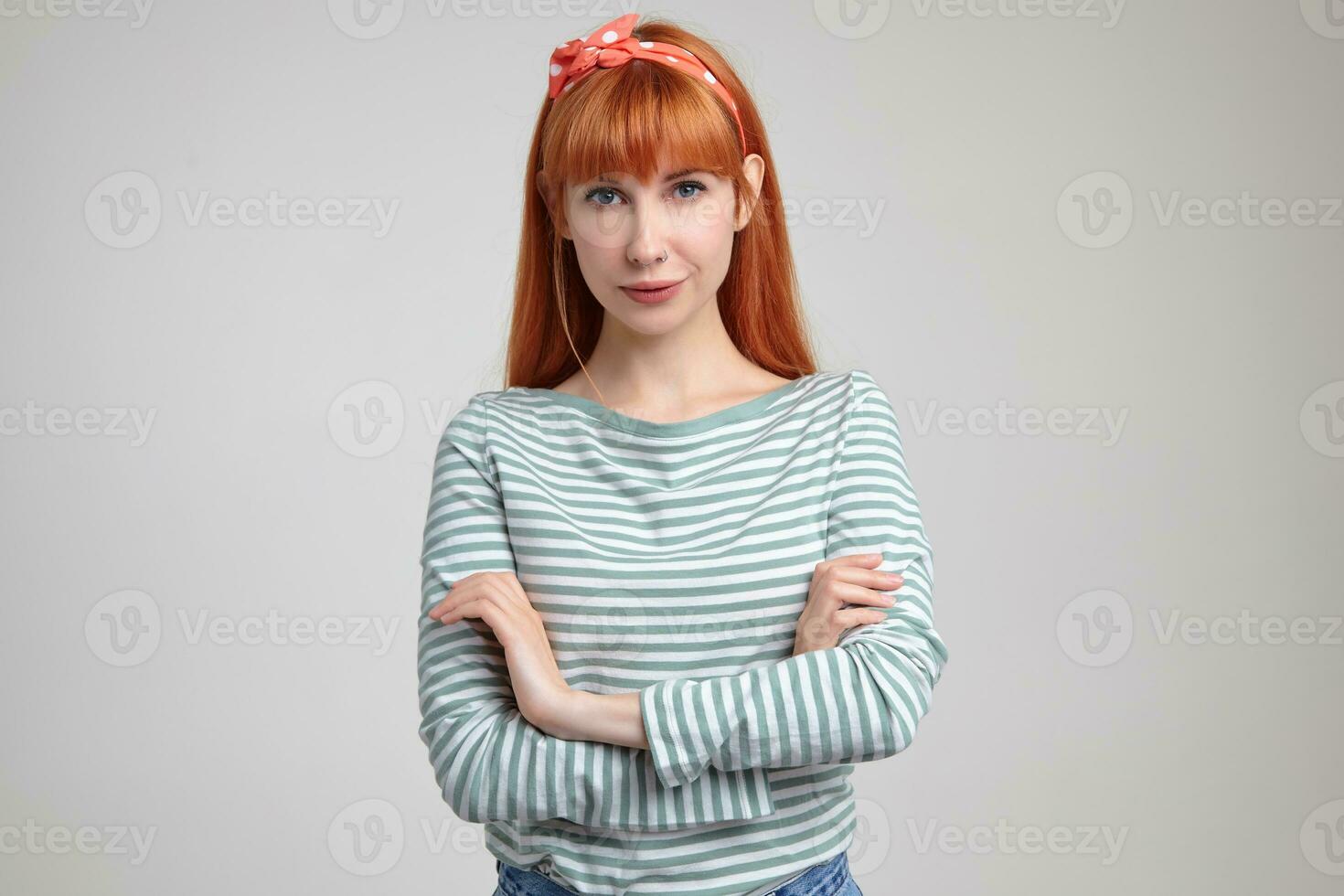 Indoor portrait of young ginger female posing over white wall looking into camera with calm facial expression photo