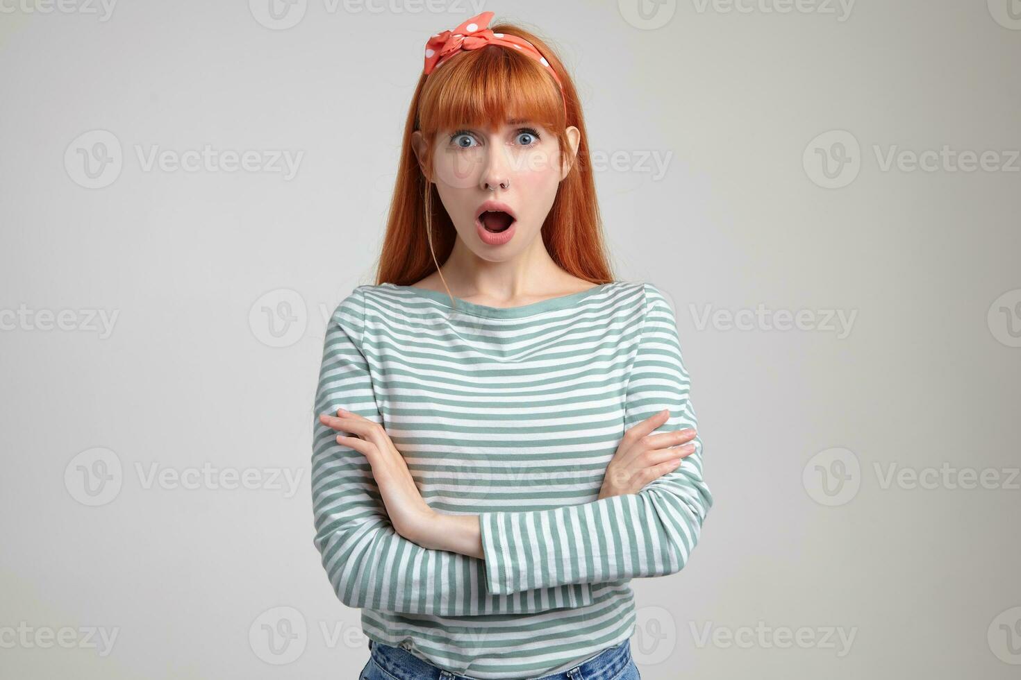 Indoor portrait of young ginger female posing over white wall looking into camera with surprised facial expression photo