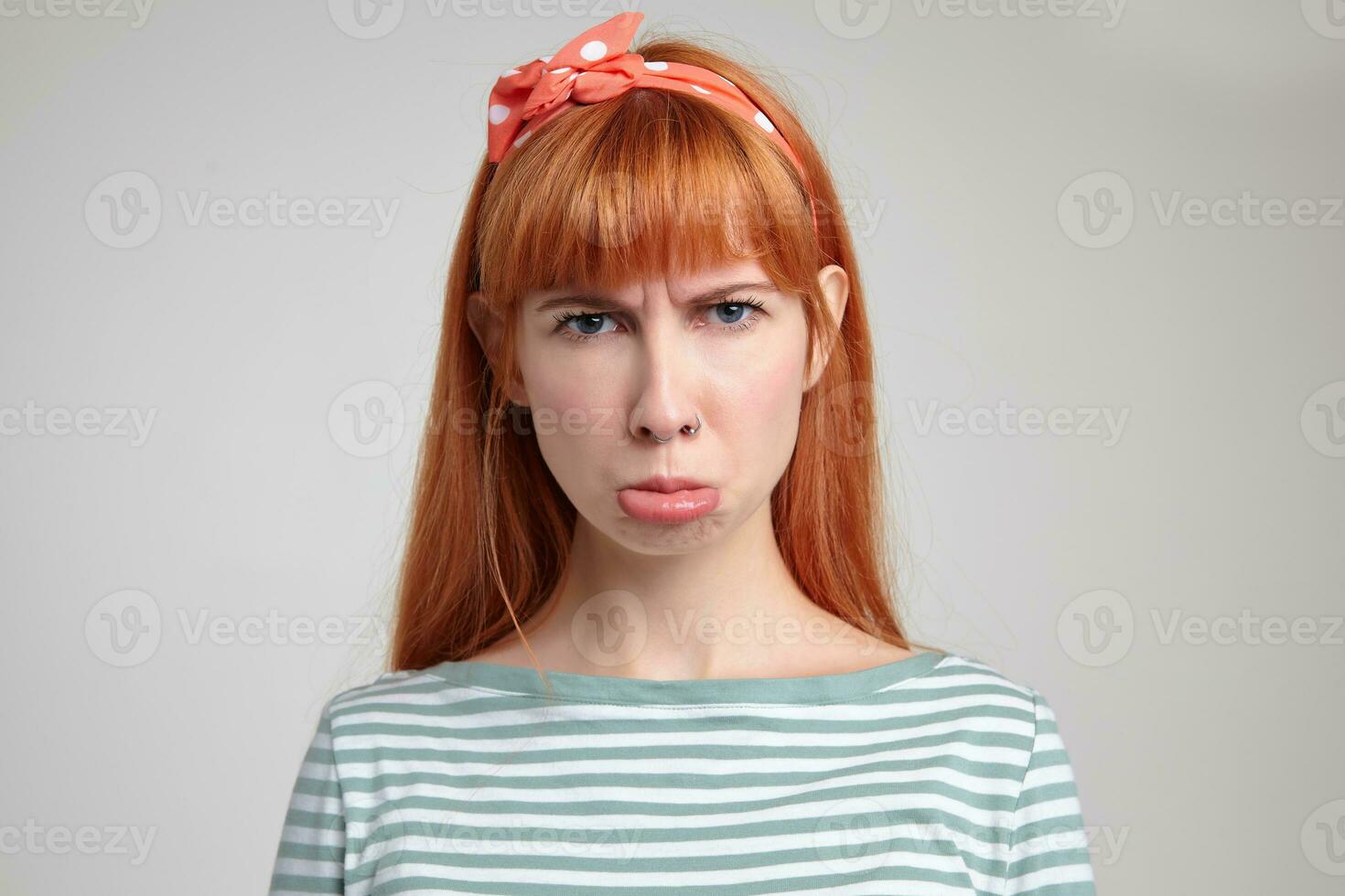 Indoor portrait of young ginger female posing over white wall curving her lip with sad facial expression photo