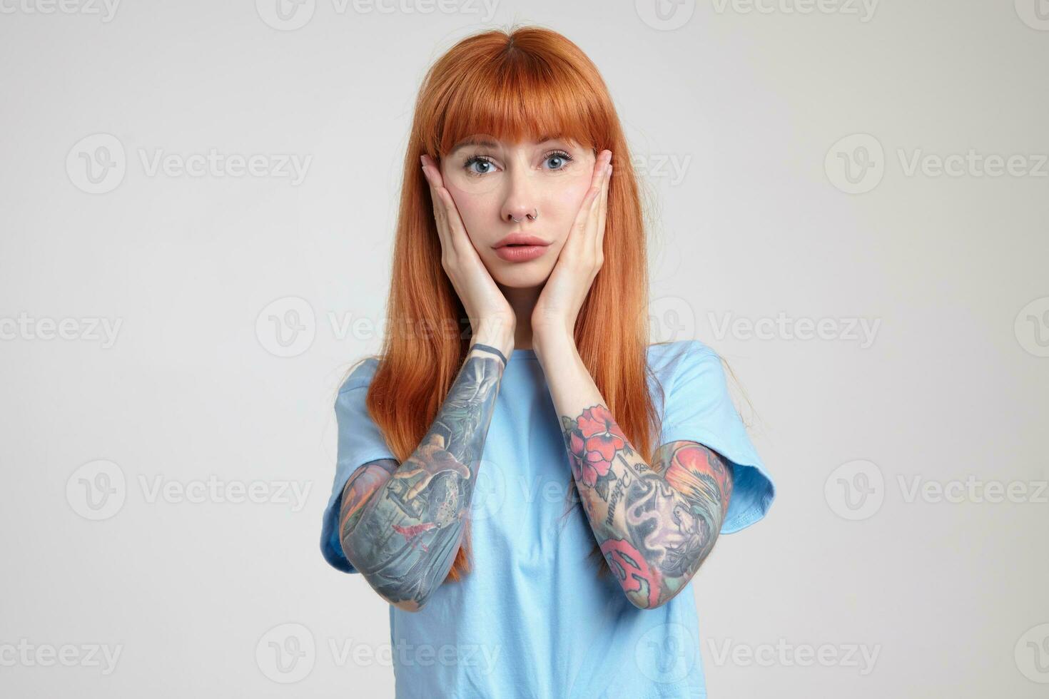 Indoor portrait of young ginger female posing over white wall looking into camera with sad facial expression photo