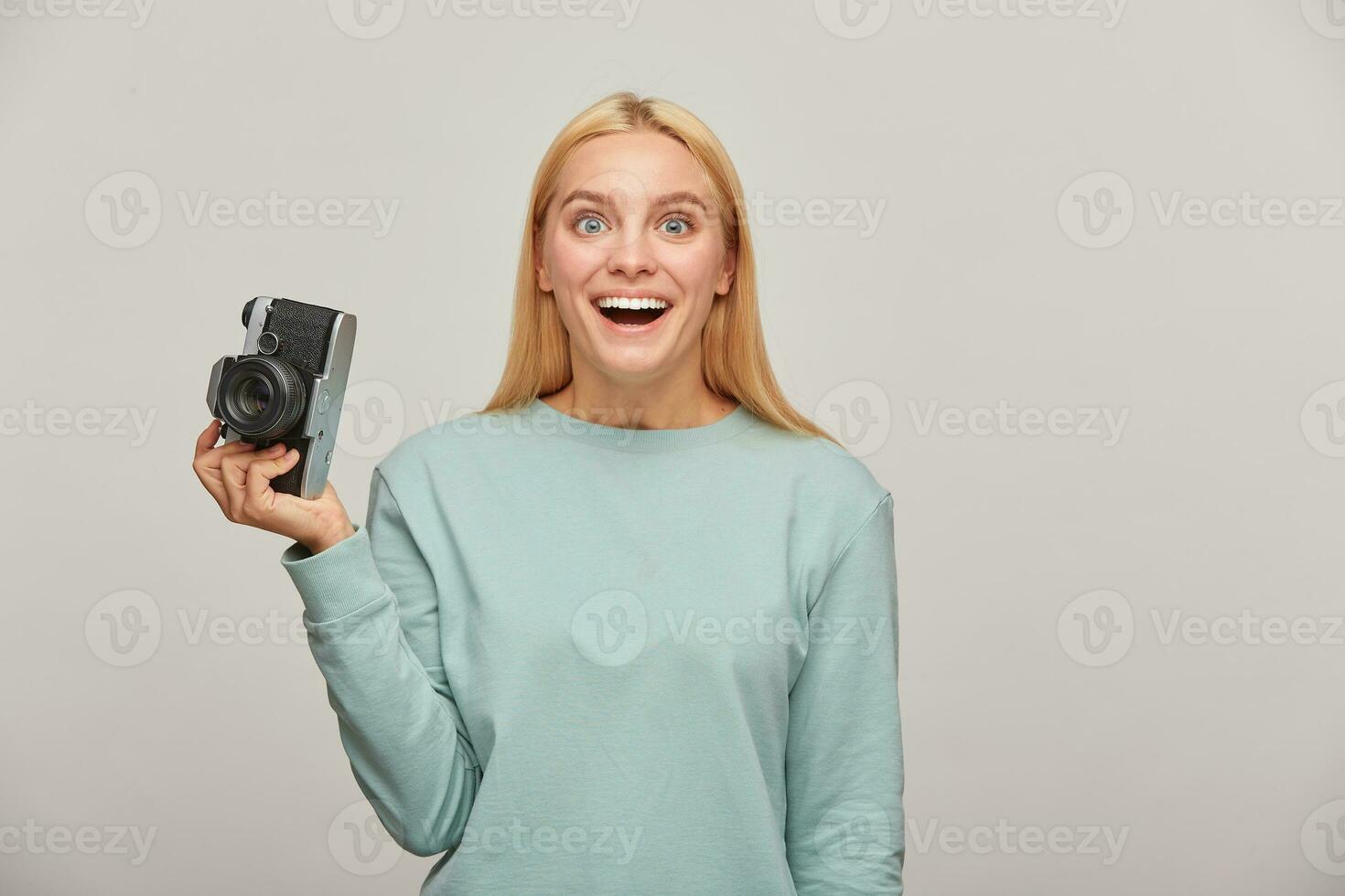 niña fotógrafo increíblemente agradablemente sorprendido ese en frente de su, qué un ver ella encontró, participación un retro Clásico foto cámara en uno mano, vistiendo azul casual camisa de entrenamiento, terminado gris antecedentes