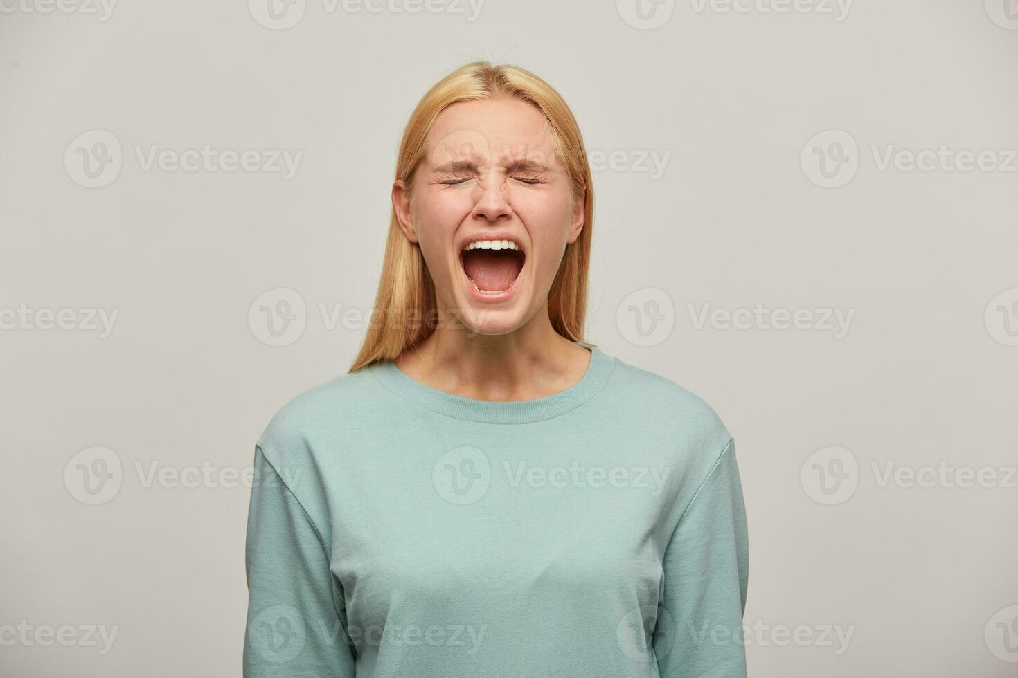 Screaming blonde girl looks frightened afraid imitate scream shout, utter a loud call or cry, an expression of a fear scare emotion, wearing blue casual sweatshirt,isolated over grey background photo